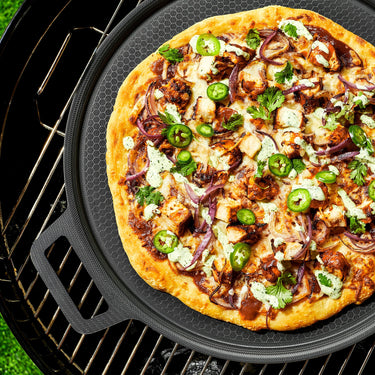 A pizza with veggies and chicken on the HexClad hybrid pizza steel, sitting on a grill